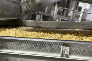 A conveyor belt loaded with golden fries, showcasing sustainable food processing practices in action.